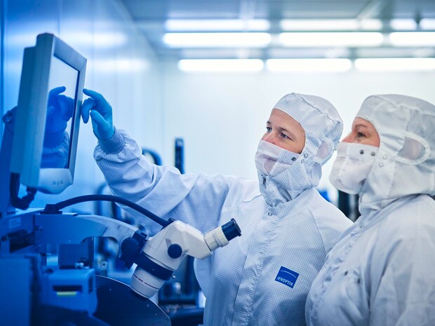 Two employees in cleanroom clothing looking at a screen