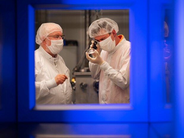 Two employees in cleanroom clothing inspect an optical system