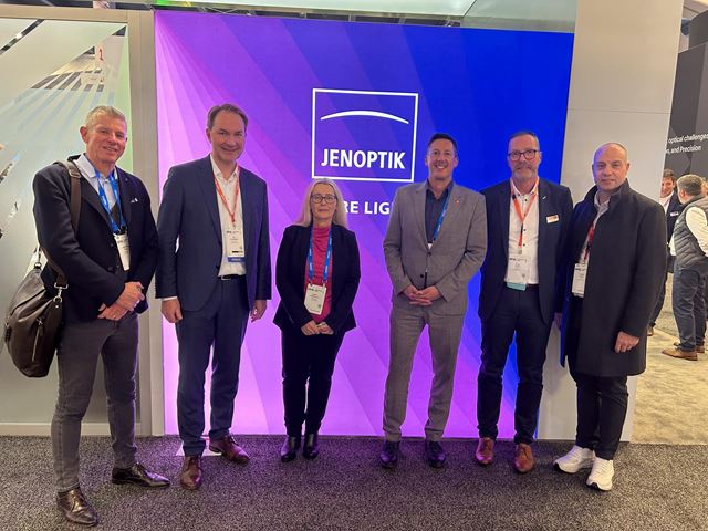 Jenoptik managers and visitors stand in front of a large colorful screen