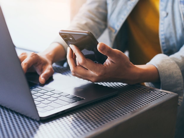 Person holding a cell phone in the left hand while typing on laptop